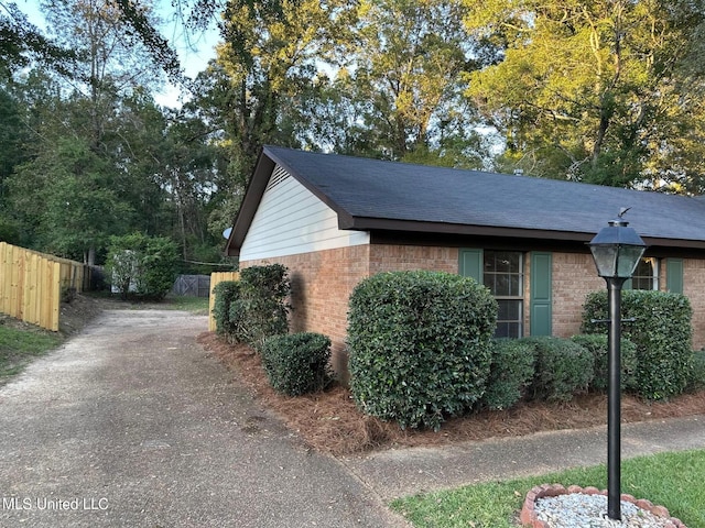 view of property exterior featuring fence, aphalt driveway, and brick siding