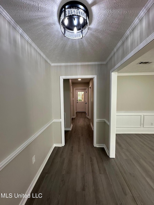 corridor featuring dark wood-type flooring, a textured ceiling, visible vents, and crown molding