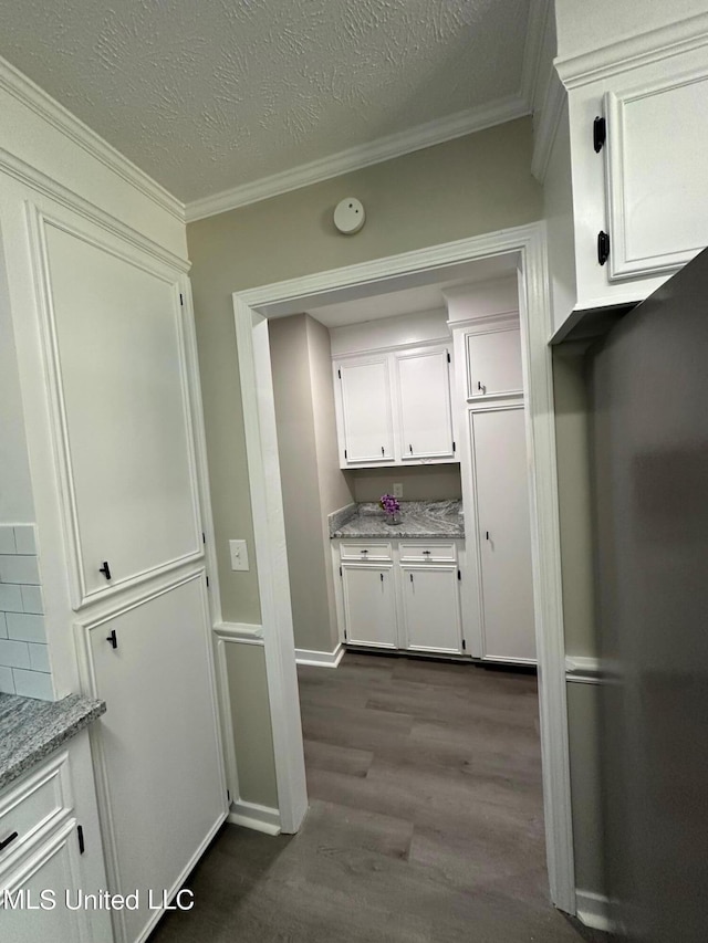 interior space with dark wood finished floors, light stone counters, crown molding, a textured ceiling, and white cabinetry