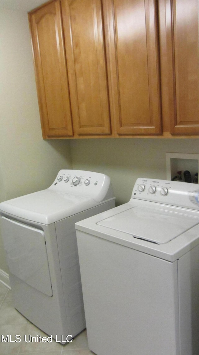 clothes washing area featuring cabinets, light tile patterned flooring, and washer and dryer