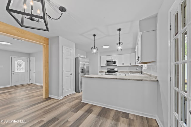 kitchen with sink, kitchen peninsula, hardwood / wood-style floors, white cabinets, and appliances with stainless steel finishes