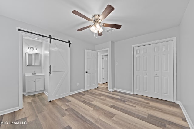 unfurnished bedroom with ensuite bath, ceiling fan, a barn door, a closet, and light wood-type flooring