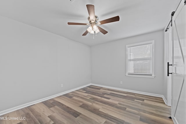 unfurnished room with wood-type flooring, a barn door, and ceiling fan