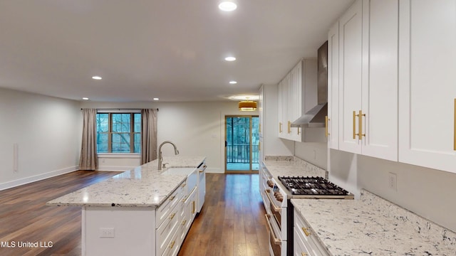 kitchen with range with two ovens, wall chimney range hood, a center island with sink, and white cabinetry