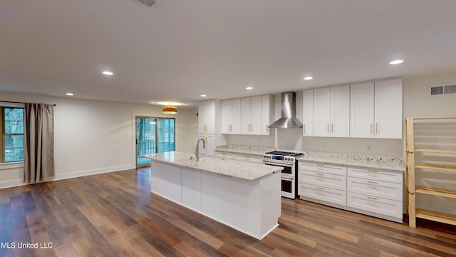 kitchen featuring wall chimney range hood, double oven range, an island with sink, and white cabinets