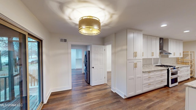 kitchen featuring wall chimney exhaust hood, white cabinetry, light stone counters, dark hardwood / wood-style flooring, and stainless steel appliances