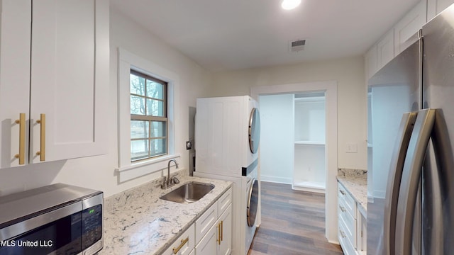 kitchen featuring stacked washing maching and dryer, sink, white cabinets, stainless steel appliances, and light stone countertops