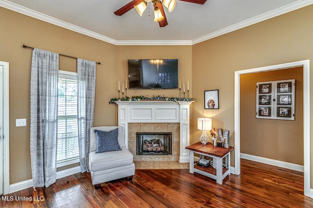 sitting room featuring ceiling fan, hardwood / wood-style flooring, a tiled fireplace, and crown molding