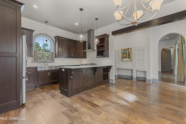 kitchen featuring a kitchen breakfast bar, sink, wall chimney exhaust hood, decorative light fixtures, and dark hardwood / wood-style flooring