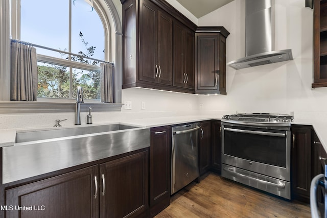 kitchen with sink, wall chimney exhaust hood, dark hardwood / wood-style floors, dark brown cabinets, and appliances with stainless steel finishes