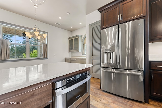 kitchen featuring light stone countertops, stainless steel appliances, an inviting chandelier, light hardwood / wood-style floors, and decorative light fixtures