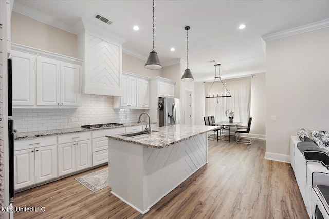 kitchen featuring white cabinets, light stone counters, an island with sink, sink, and stainless steel appliances