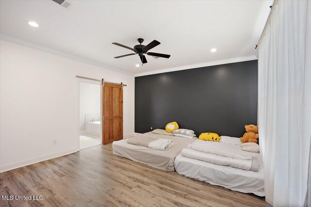 bedroom with light hardwood / wood-style floors, a barn door, connected bathroom, and ceiling fan