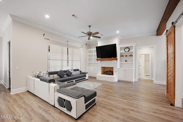 living room with a barn door, a stone fireplace, light hardwood / wood-style floors, and ceiling fan