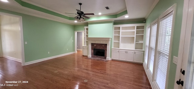 unfurnished living room with hardwood / wood-style floors, crown molding, ceiling fan, a fireplace, and a tray ceiling