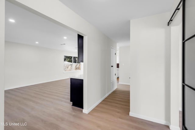 hall featuring baseboards, a barn door, recessed lighting, and light wood-style floors