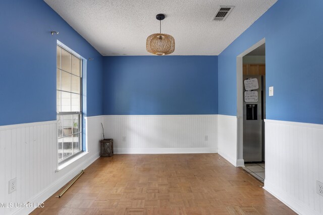 spare room featuring a wainscoted wall, visible vents, and a textured ceiling