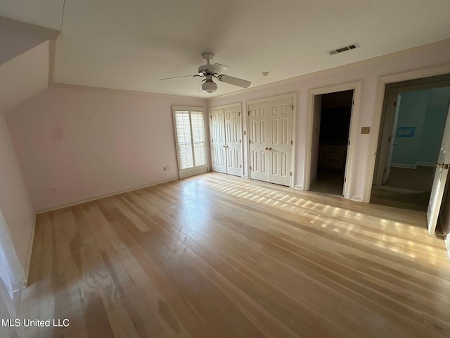 unfurnished bedroom with ceiling fan, ensuite bath, light wood-type flooring, and two closets