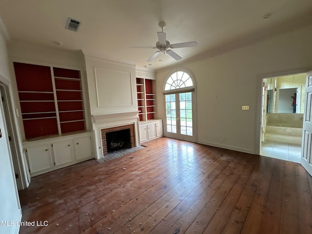 unfurnished living room featuring ceiling fan, a fireplace, wood-type flooring, built in features, and french doors