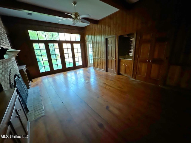 unfurnished living room with wooden walls, hardwood / wood-style floors, ceiling fan, and a brick fireplace