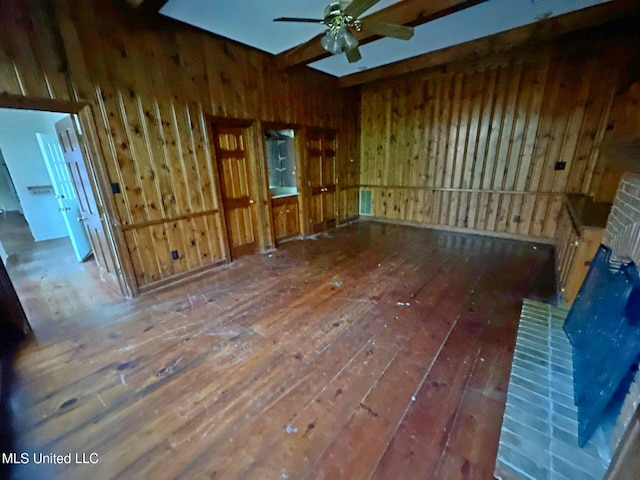 unfurnished room featuring wood walls, wood-type flooring, ceiling fan, and a fireplace