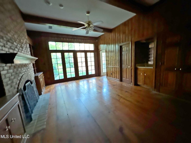 living room featuring a brick fireplace, light wood-type flooring, beamed ceiling, and ceiling fan