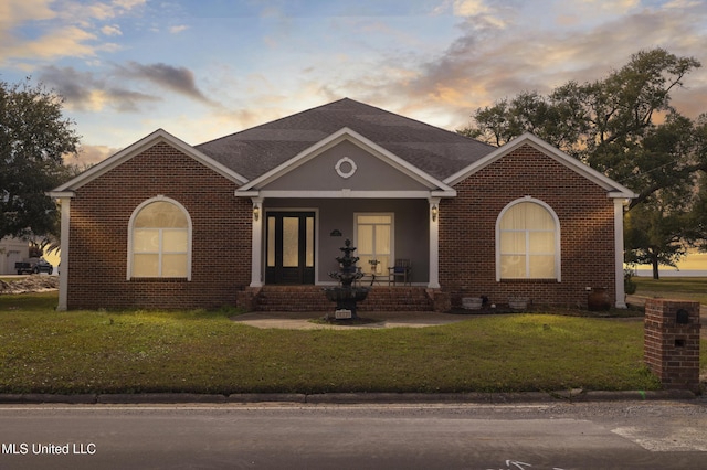 view of front of house with brick siding, a shingled roof, and a yard