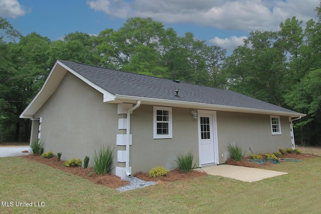 back of house with a lawn, stucco siding, and roof with shingles