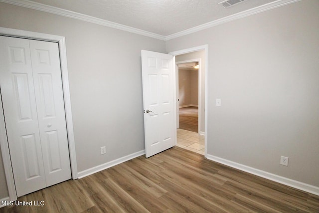unfurnished bedroom featuring baseboards, ornamental molding, wood finished floors, and a closet
