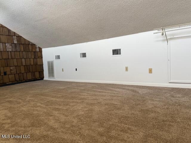 unfurnished room with a textured ceiling, carpet, baseboards, vaulted ceiling, and visible vents