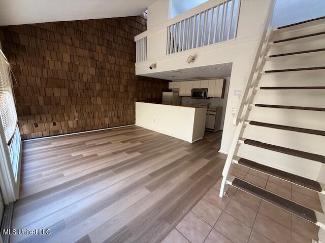 unfurnished living room with tile patterned floors, stairs, and high vaulted ceiling
