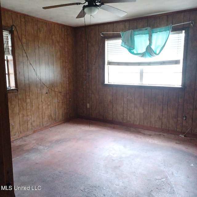 empty room featuring a wealth of natural light, ceiling fan, and wood walls