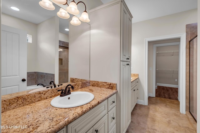 full bath featuring an inviting chandelier, vanity, a tile shower, and a walk in closet