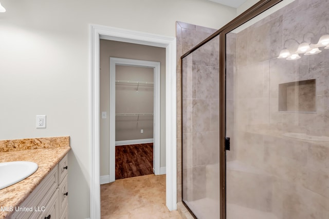 full bathroom featuring vanity, baseboards, a shower stall, and a walk in closet