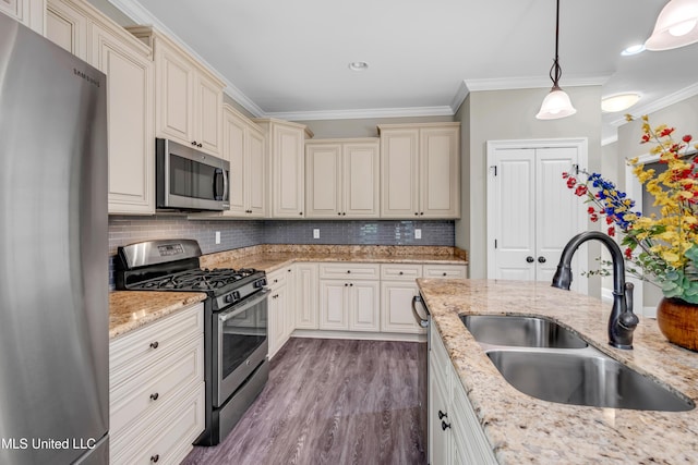 kitchen with cream cabinets, appliances with stainless steel finishes, a sink, wood finished floors, and ornamental molding