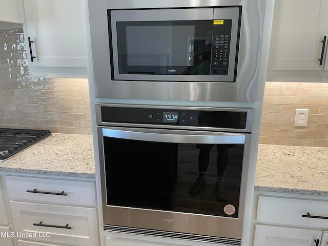 interior details with white cabinets, backsplash, stainless steel appliances, and light stone countertops