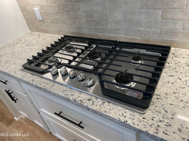 room details with light stone countertops, white cabinetry, and stainless steel gas stovetop