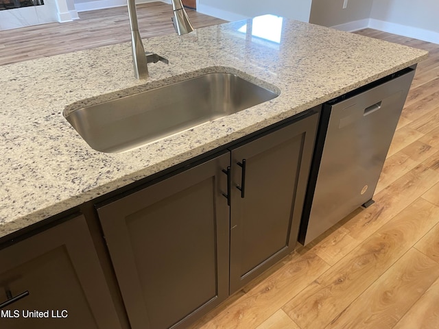 kitchen with light stone countertops, light hardwood / wood-style flooring, stainless steel dishwasher, and sink