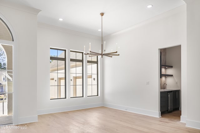 unfurnished dining area featuring a notable chandelier, crown molding, sink, and light hardwood / wood-style flooring