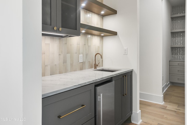 kitchen featuring decorative backsplash, stainless steel fridge, light stone counters, sink, and light hardwood / wood-style floors