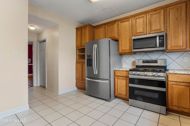 kitchen with light stone counters, stainless steel appliances, tasteful backsplash, and light tile patterned floors