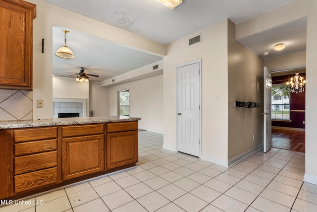 kitchen with backsplash, light tile patterned floors, a textured ceiling, ceiling fan with notable chandelier, and light stone counters