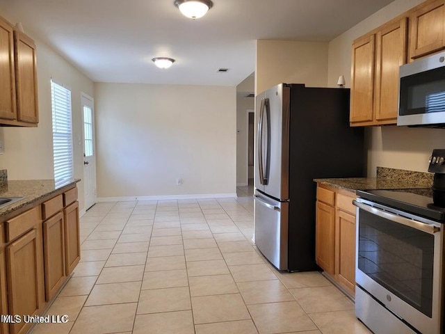 kitchen with light tile patterned floors, brown cabinetry, baseboards, dark stone counters, and appliances with stainless steel finishes