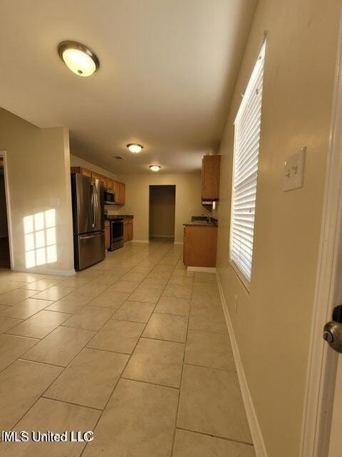 kitchen featuring light tile patterned floors, baseboards, brown cabinets, and appliances with stainless steel finishes