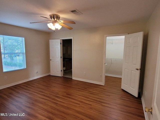 unfurnished bedroom with wood finished floors, a spacious closet, visible vents, and baseboards