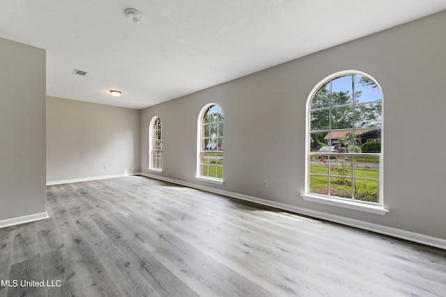 empty room featuring visible vents, baseboards, a textured ceiling, and wood finished floors