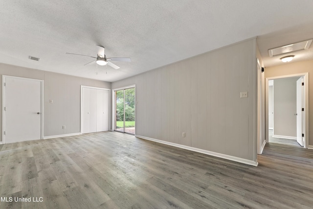 spare room with a textured ceiling, a ceiling fan, visible vents, wood finished floors, and baseboards