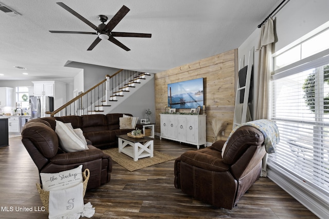 living area featuring visible vents, a textured ceiling, dark wood finished floors, stairway, and wooden walls