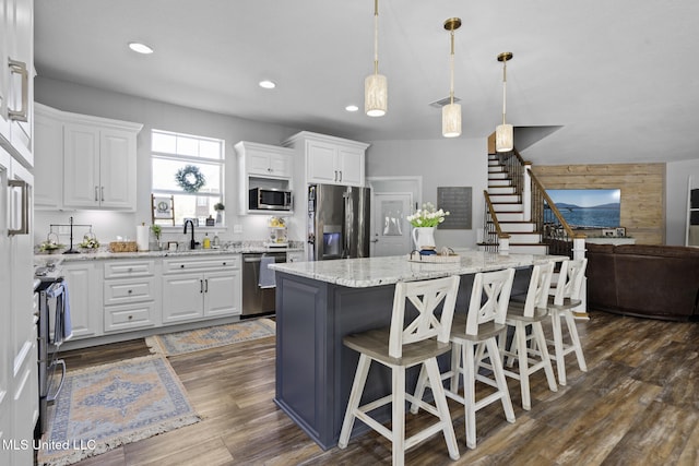 kitchen featuring a sink, a kitchen island, open floor plan, stainless steel appliances, and white cabinets