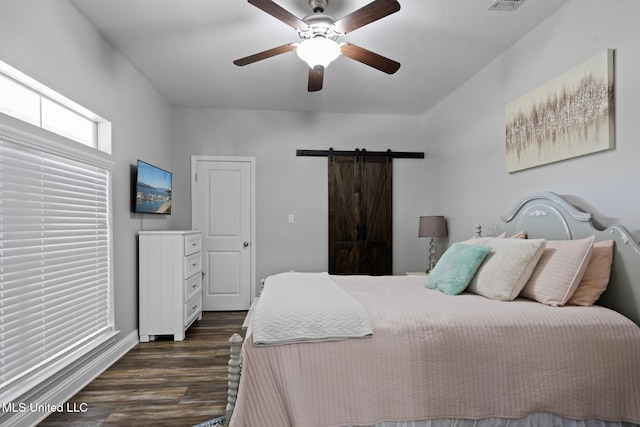 bedroom with ceiling fan, a barn door, visible vents, and dark wood finished floors